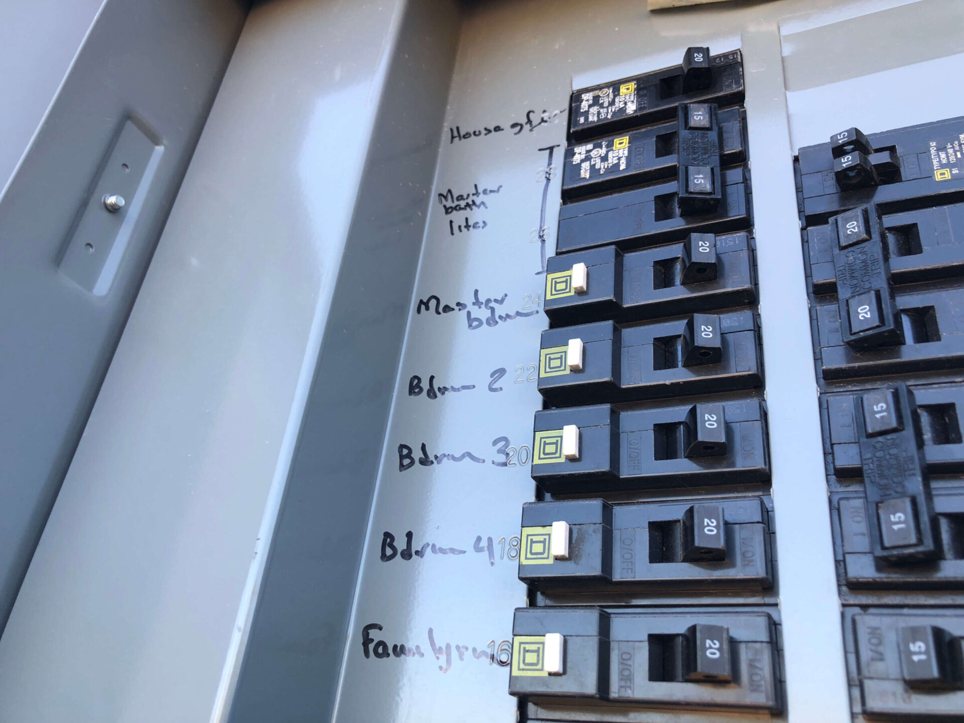 An electrical panel with handwritten labels for circuit breakers indicating various rooms like bedrooms and master bath. Circuit breakers are numbered with amperages visible.
