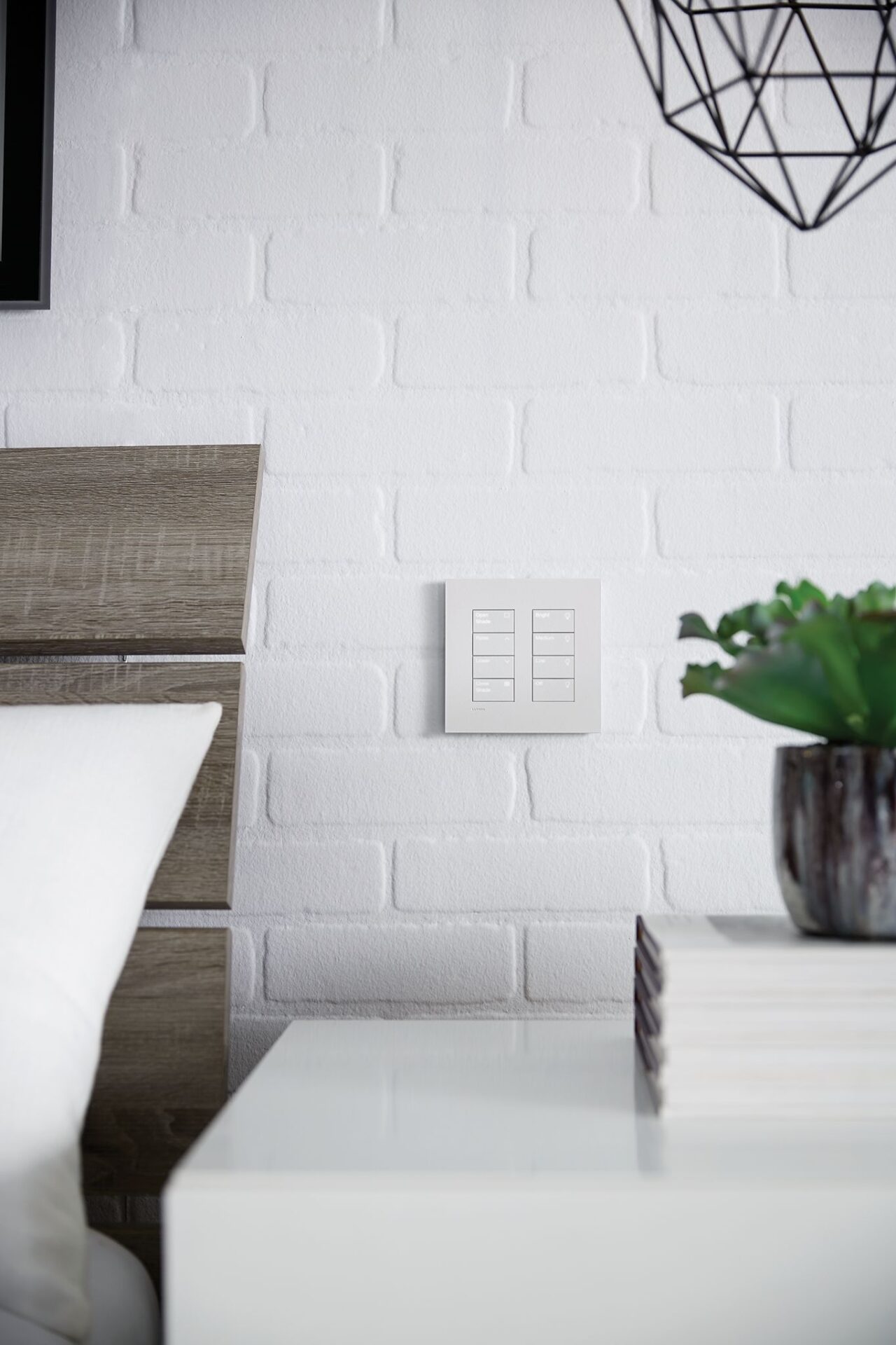 Modern interior with a white brick wall, wooden furniture, a geometric light fixture, light switch plates, a pillow, and a potted plant on a nightstand.