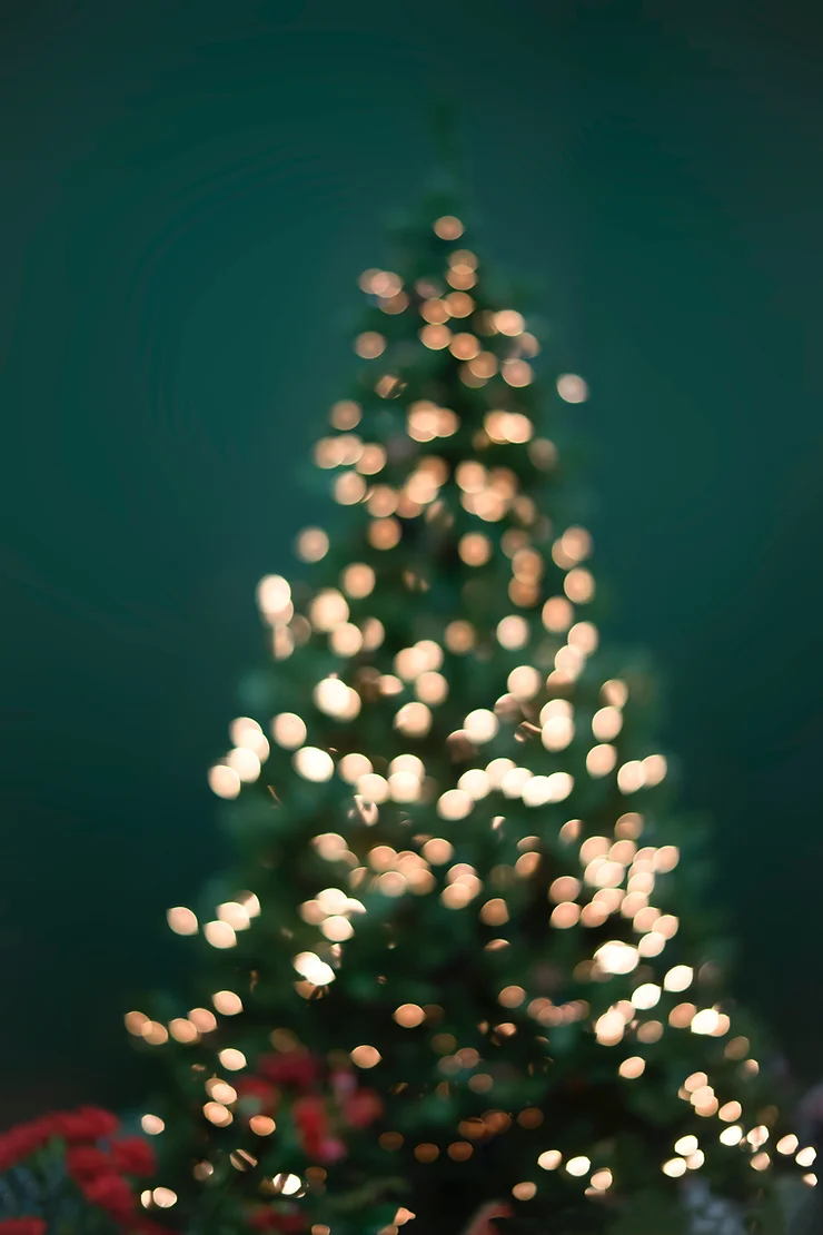 This is a blurred image of a Christmas tree with glowing lights on a dark green background, creating a festive, bokeh effect.
