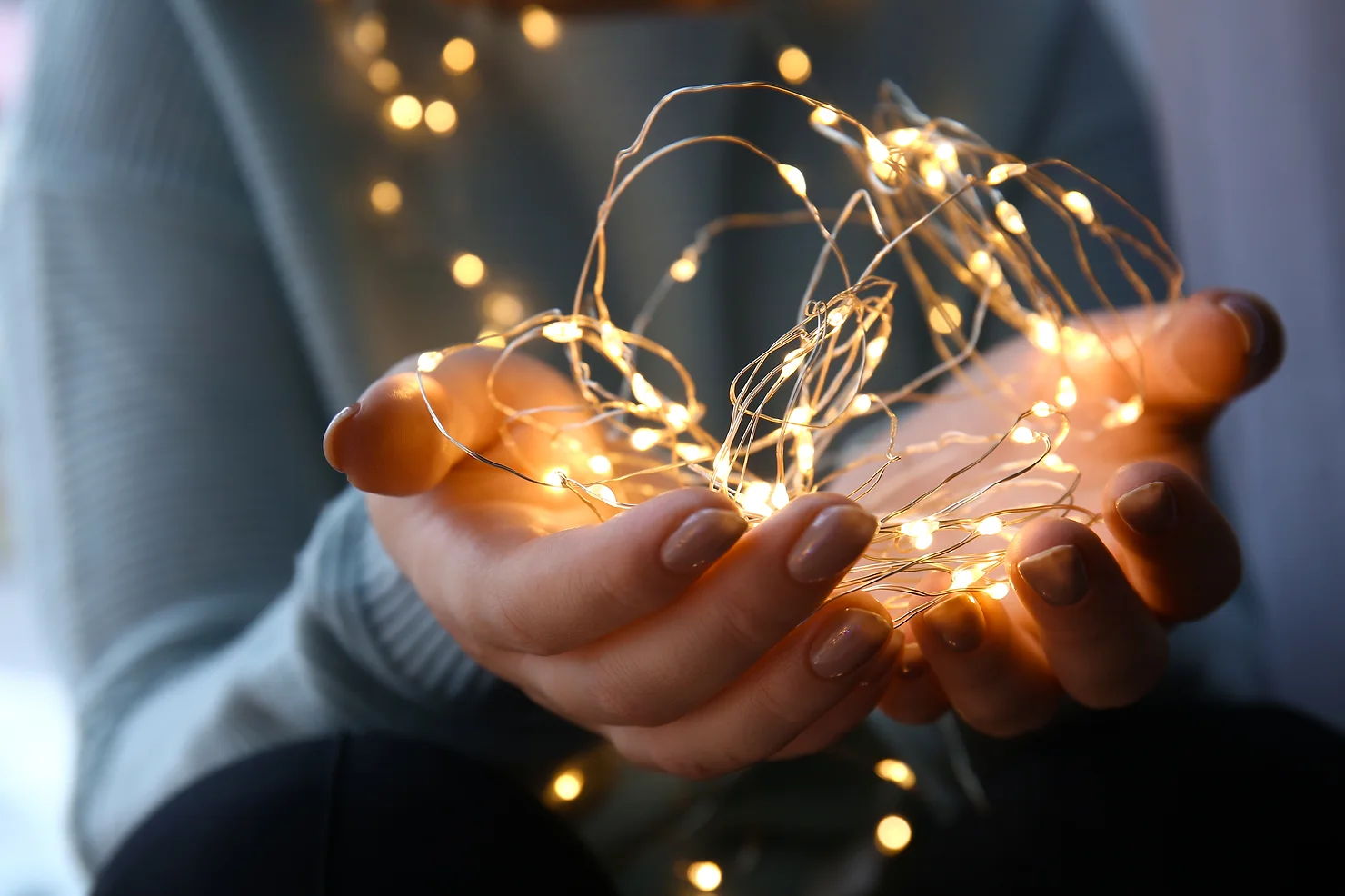 A person is holding a warm, glowing string of LED fairy lights gently in their hands, creating a cozy and magical atmosphere.